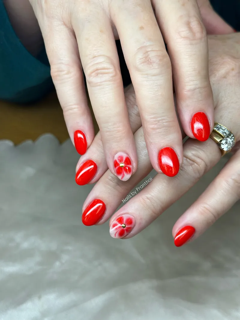 Glossy red almond nails with two hand-painted floral feature nails